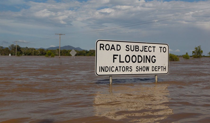 Flooded road in Australia, submerged sign reading "Road subject to flooding"