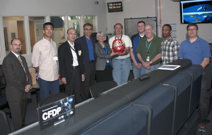 In the Mission Operations Center on May 16, 2014, GPM's NASA and Japan Aerospace Exploration Agency project managers deliver the completed Daruma doll 